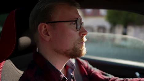 un joven con barba y gafas conduce un auto, toma de cerca dentro del auto