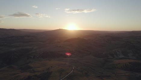 Drone-flying-sideways-filming-a-Italian-landscape-with-hills,-trees-and-fields-of-grass-at-sunrise-in-4k