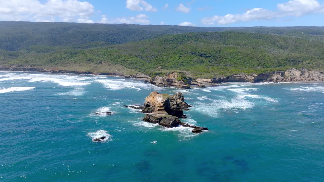 Ripresa aerea in parallasse attorno a una formazione rocciosa con le onde dell'Oceano Pacifico che si infrangono e la Riserva Costiera Valdiviana sullo sfondo in Cile