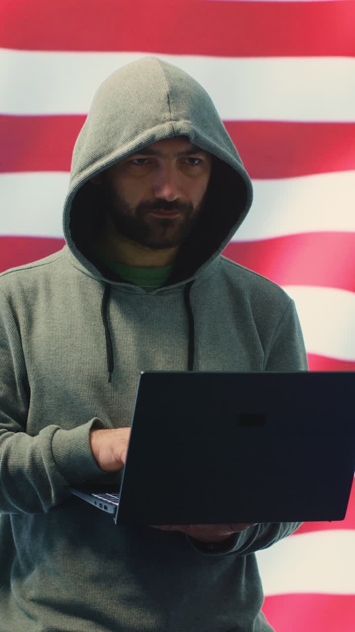 Uomo con felpa con cappuccio che digita su un laptop davanti alla bandiera americana