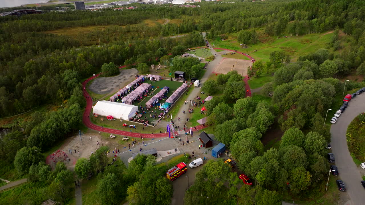 Aerial drone view of the Relay for Life cancer fundraising event in Tromsø, Norway. Participants walk around a track surrounded by tents and green forest during the community gathering