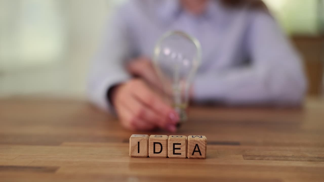 Wooden blocks spelling IDEA with a person holding a light bulb