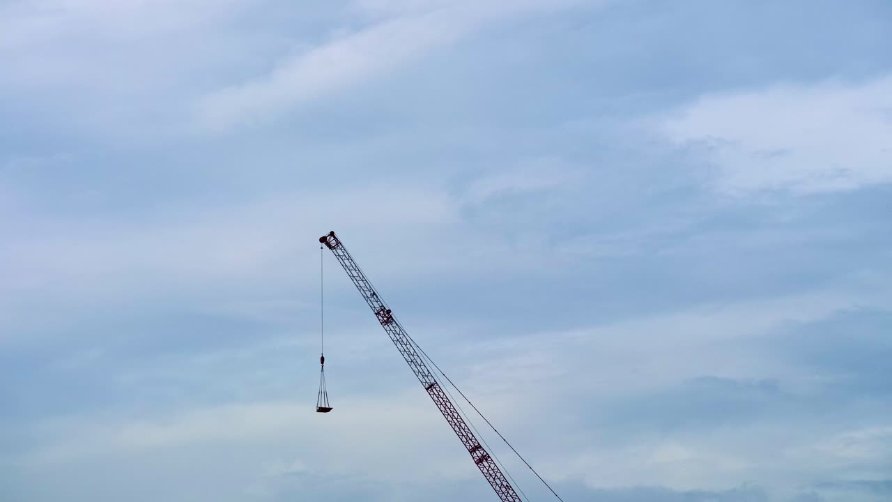 A red and white tower crane at a construction site against a cloudy sky over the city