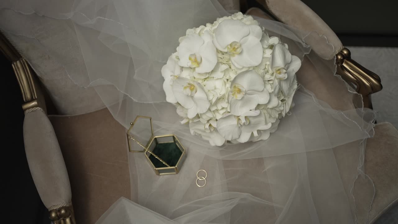Elegant bridal bouquet on veil draped chair with wedding rings and box