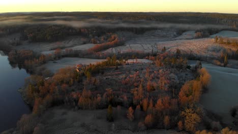 Aerial-view-of-a-countryside-field-near-a-lake-at-dawn-with-low-fog-in-autumn