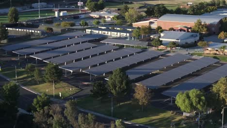 Sobrevuelo-Aéreo-De-Drones-Sobre-La-Red-De-Paneles-Solares-Sostenibles-En-El-Estacionamiento-De-La-Escuela,-4k