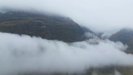 Misty-Glencoe-mountains-shrouded-in-thick-clouds-on-a-foggy-day,-aerial-view