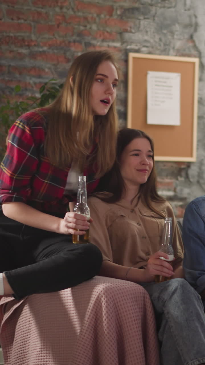 Group of emotional multinational friends watches football championship and drinks beer in apartment slow motion. Dangerous moments during important match