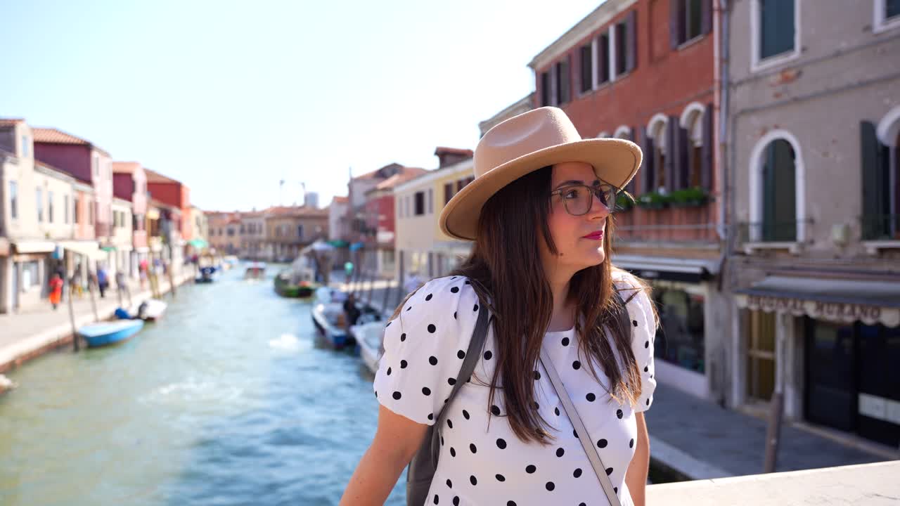 Female tourist with hat enjoys sun on bridge over Canal in Murano, Italy
