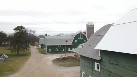 american flag waving with green barn in background drone video