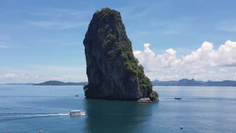 Famous-limestone-cliff-protruding-from-ocean-as-speedboat-passes-by,-Koh-Poda,-Krabi