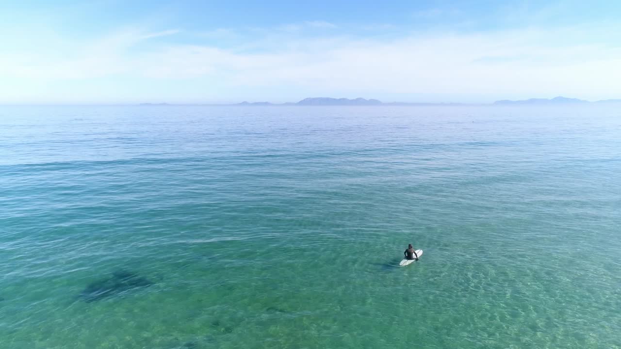 파도를 기다리는 물 속에서 서핑보드에 앉아 있는 남자의 정적인 공중 전망