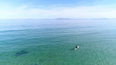 vista aérea estática de un tipo sentado en su tabla de surf en el agua esperando olas
