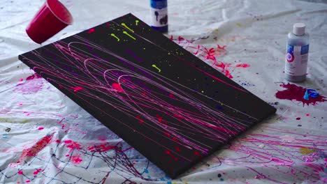 paint pendulum swings back and forth across a black canvas covered in neon paint