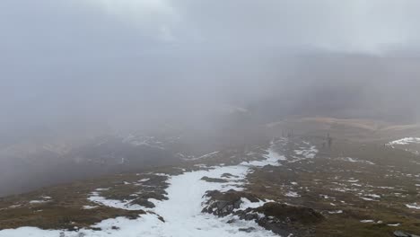 Slow-panning-shot-of-hikers-descending-down-Ben-Lomond-with-snowy-trails-in-mist