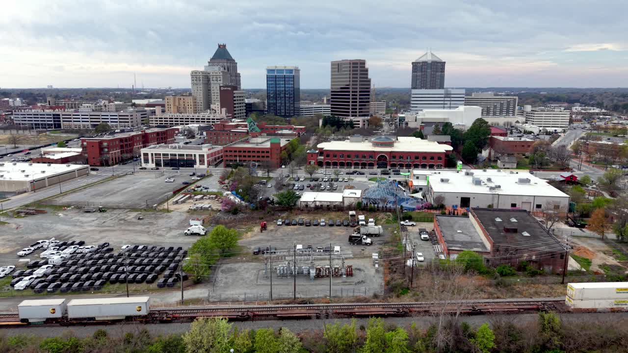Inquadratura aerea in avvicinamento allo skyline di Greensboro oltre un treno merci.