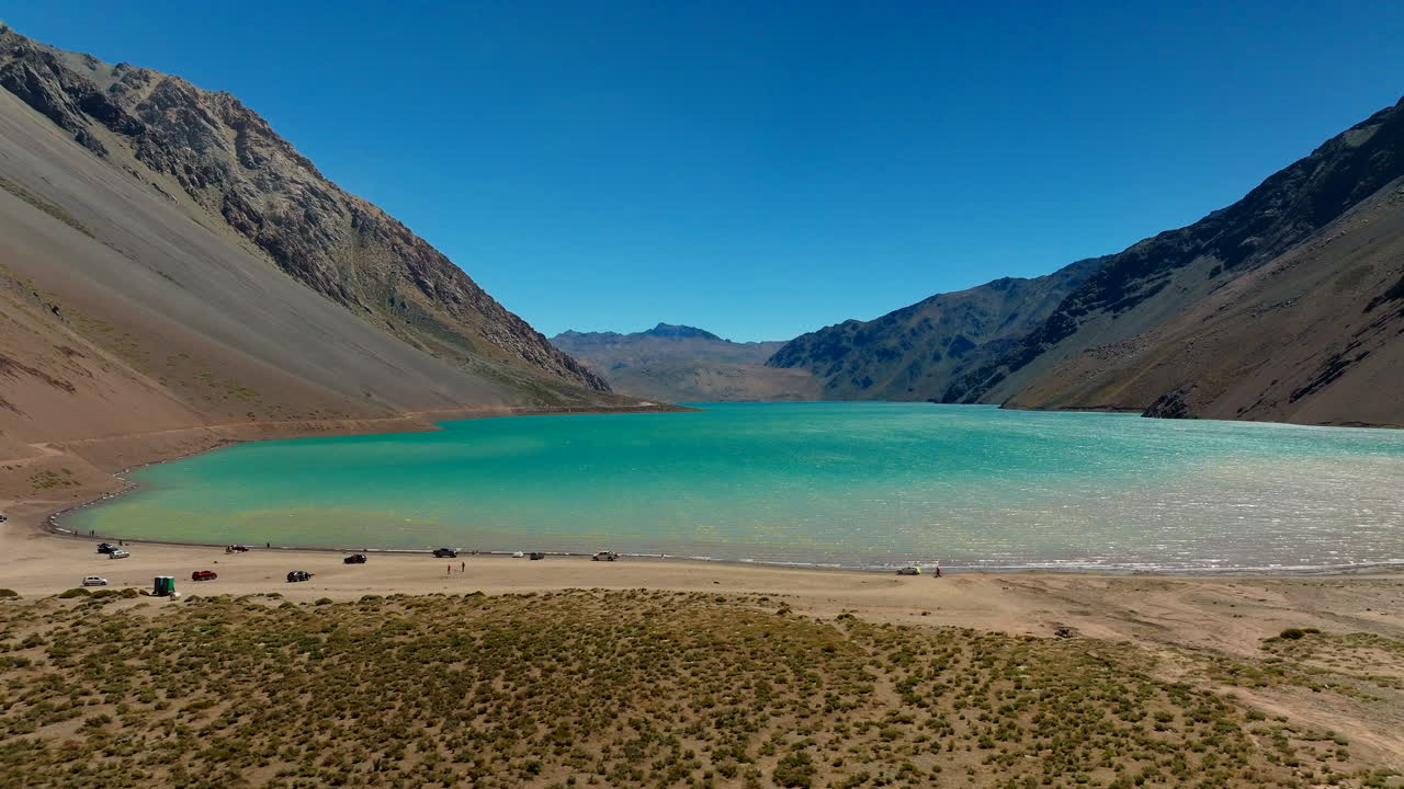 Car driving near vibrant blue water and arid mountains in Chile’s Cajon del Maipo region, visiting stunning desert lake