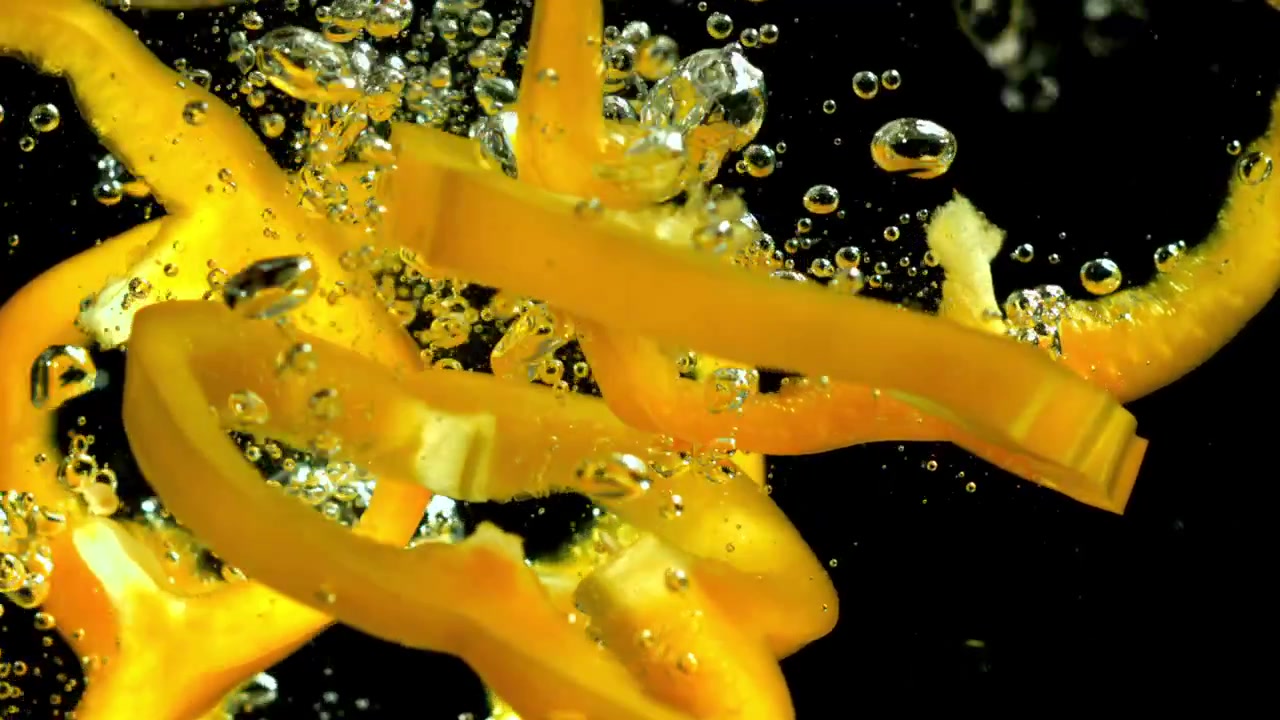Fette di peperone giallo fresco che schizzano nell'acqua al rallentatore