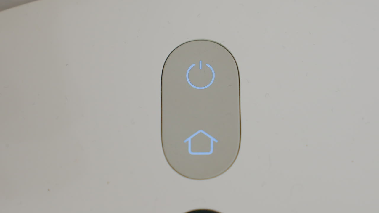 Close up of robot vacuum cleaner showing illuminated power and home button glowing blue on control panel, highlighting modern design, and intelligent smart home cleaning technology