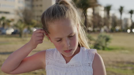 retrato de una niña caucásica linda corriendo de la mano a través del cabello buscando serio en el parque urbano al atardecer en cámara lenta