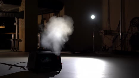a fog machine creating smoke under a spotlight in a dark room