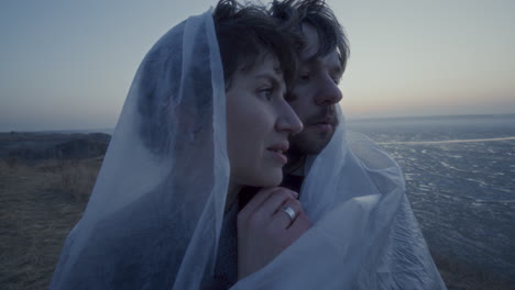 romantic couple wrapped in sheer fabric looking over frozen lake