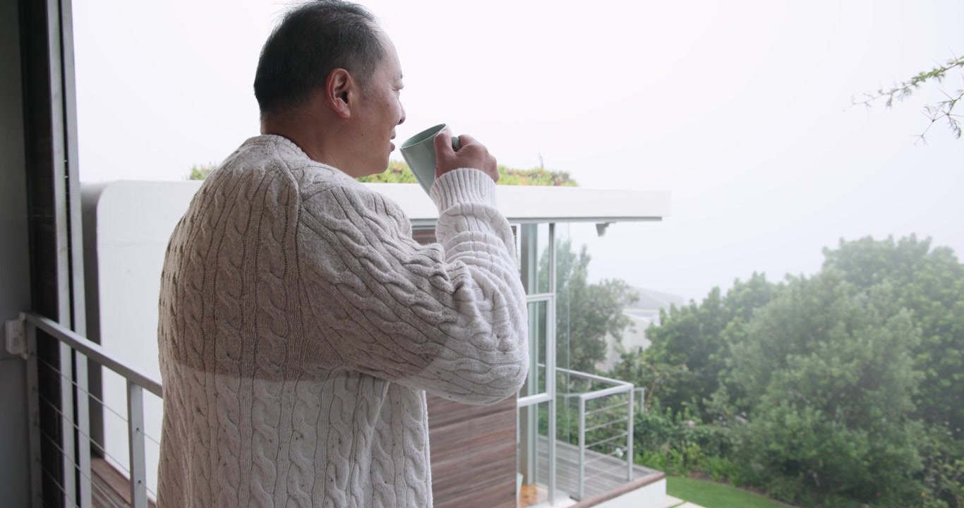 Anziano uomo cinese che si affaccia alla porta, sorseggiando da una tazza verde, appoggiato alla ringhiera del balcone e che contempla, con spazio per il testo.