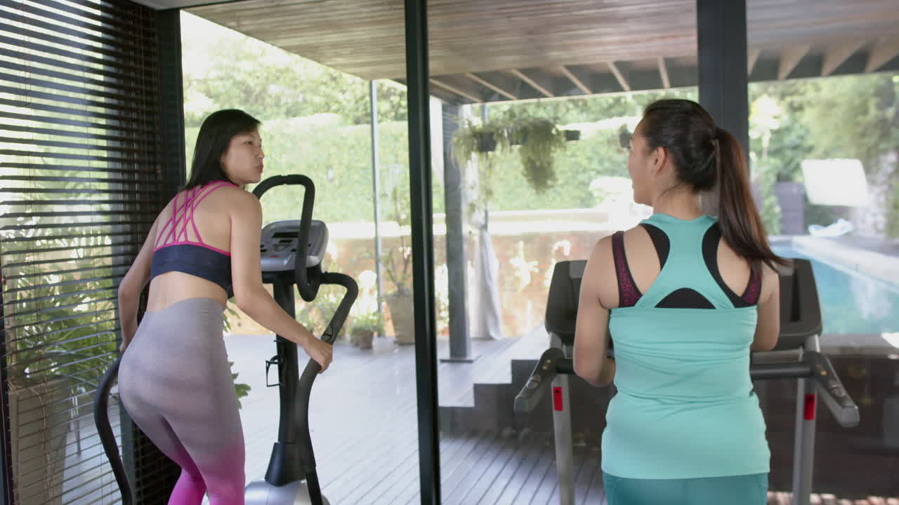 amigas asiáticas felices haciendo ejercicio y discutiendo en el gimnasio de casa soleado, cámara lenta