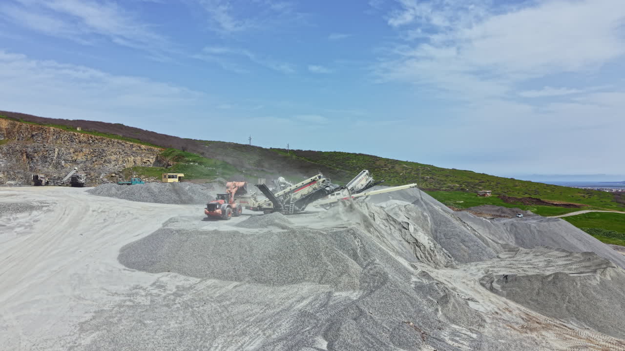 Granitbruddrift med tungt maskineri, der arbejder på en grusplads om dagen.