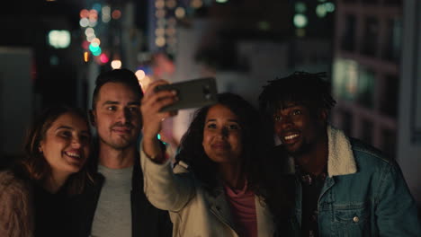 Junge-Multiethnische-Freunde-Posieren-Nachts-Auf-Dem-Dach-Für-Ein-Gruppenfoto-Und-Feiern-Ein-Freundschaftstreffen.-Junge-Frau-Nutzt-Ihr-Smartphone-Und-Teilt-Ihr-Wochenendtreffen-In-Den-Sozialen-Medien