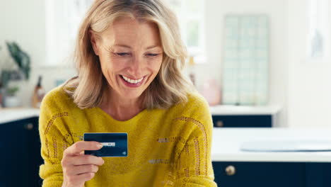 close up of mature woman with credit card using digital tablet at home to book holiday or shop