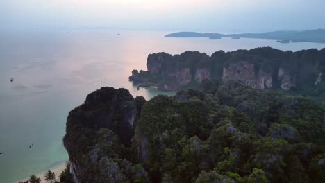 railay beach with traditional longtail boats dotting the andaman sea, surrounded by towering limestone cliffs at sunrise, krabi, thailand. amazing aerial view flight panorama overview drone