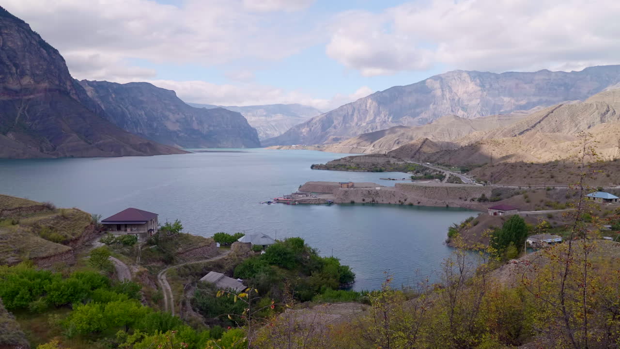 Fjellfjordlandsby innrammet av robuste topper, stille vann, spredte hus, svingete sti, myk sky