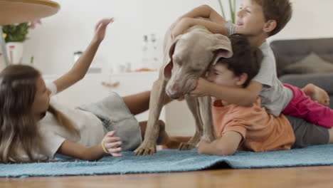 Niños-Felices-Tirados-En-El-Suelo-Y-Jugando-Con-El-Perro-En-Casa