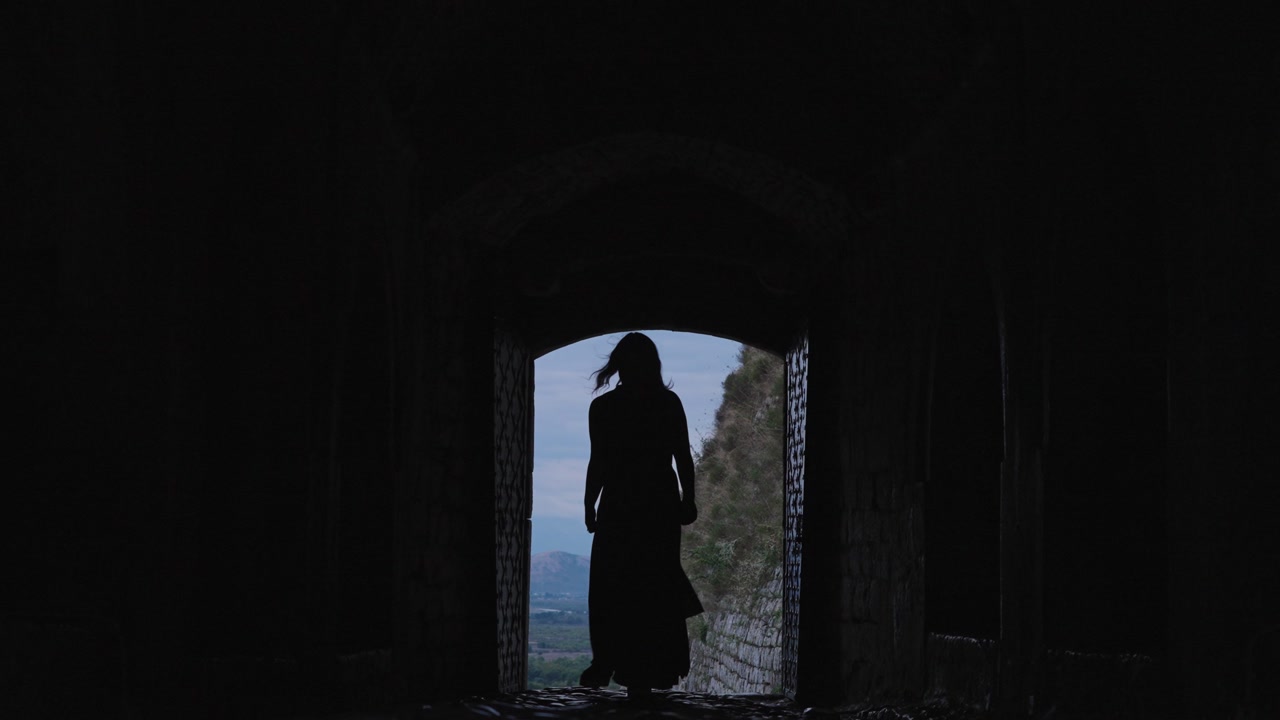 Silhouette of woman walking through tunnel at Rozafa Castle, Albania. Static wide shot, backlit