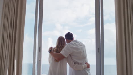 happy-travel-couple-on-honeymoon-vacation-looking-out-window-enjoying-beautiful-view-of-ocean-at-embracing-sharing-romantic-holiday