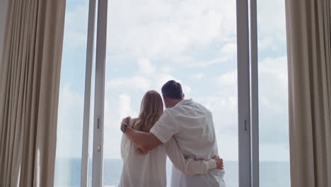 happy travel couple on honeymoon vacation looking out window enjoying beautiful view of ocean at embracing sharing romantic holiday