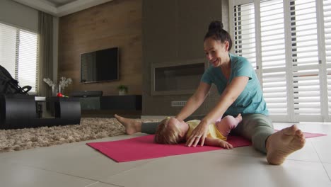 caucasian mother playing with her baby while practicing yoga on yoga mat at home