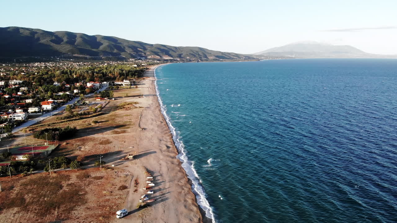 View of Aegean sea coast in Asprovalta at sunset from the drone. Multiple buildings and greenery. Rough sea, waves with foam. Greece