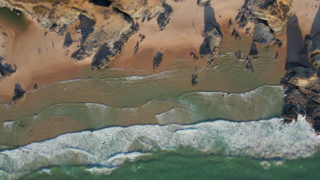 Aerial-view-of-Praia-do-Banho-with-waves-breaking,-in-the-town-of-Porto-Covo,-Portugal