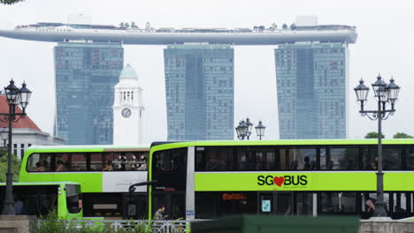 green buses passing in front of singapore’s iconic skyline with marina bay sands in the background