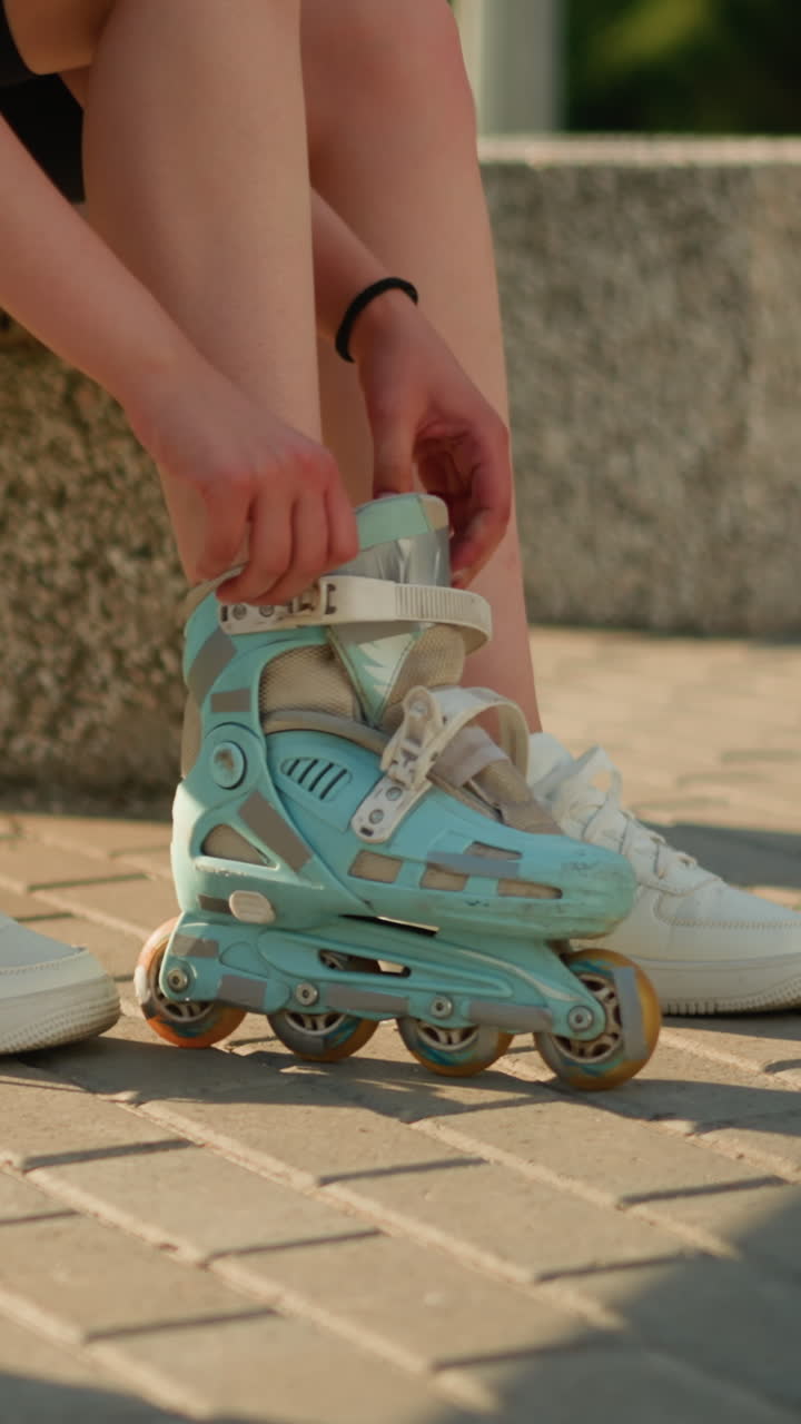 Side view of individual seated on bench wearing roller skate on left leg while right leg wears sneaker, with sneaker placed nearby, sunlight casts warm shadows on interlocked pavement