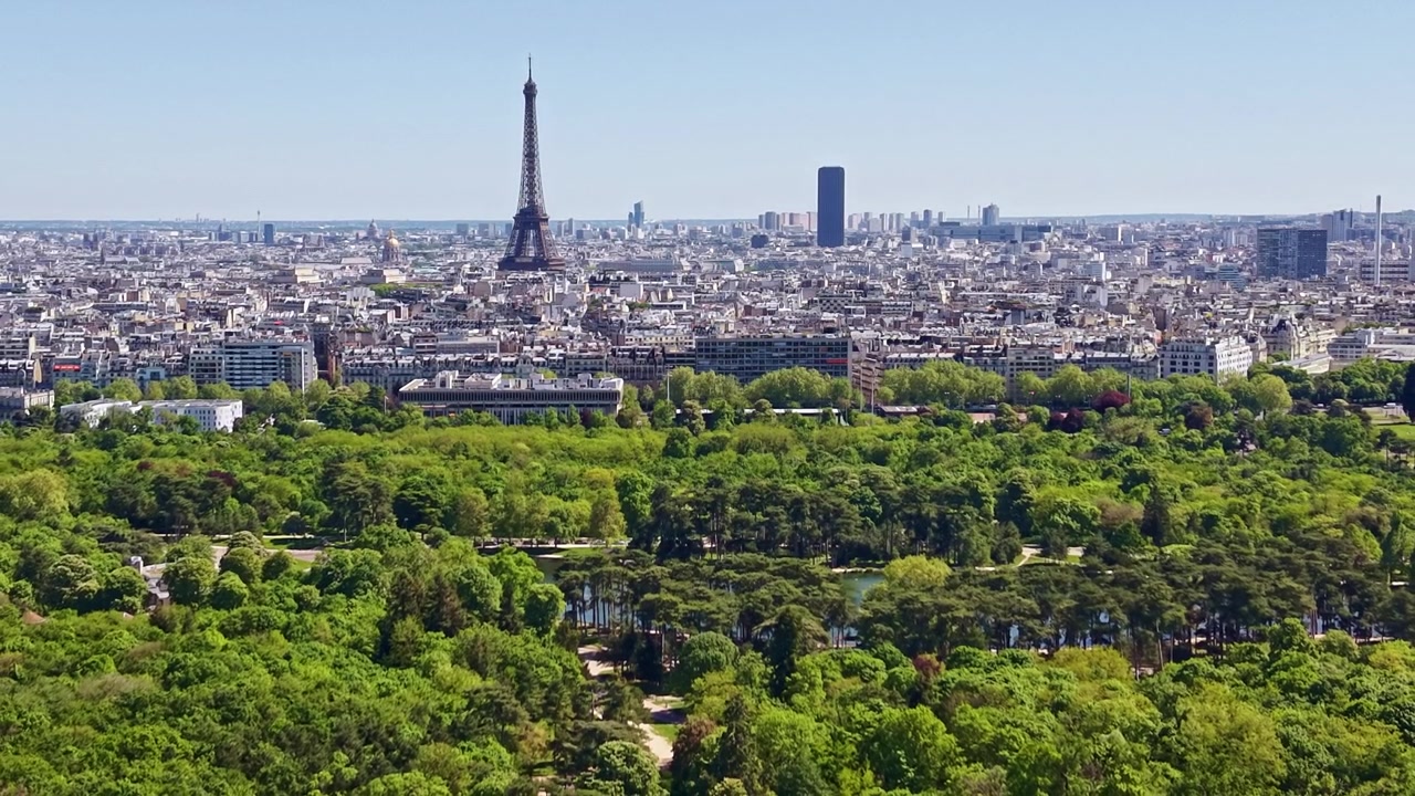 Vista aerea dall'alto del Bois de Boulogne in contrasto con il denso skyline di Parigi, la Torre Eiffel e il quartiere degli affari de La Défense in lontananza.