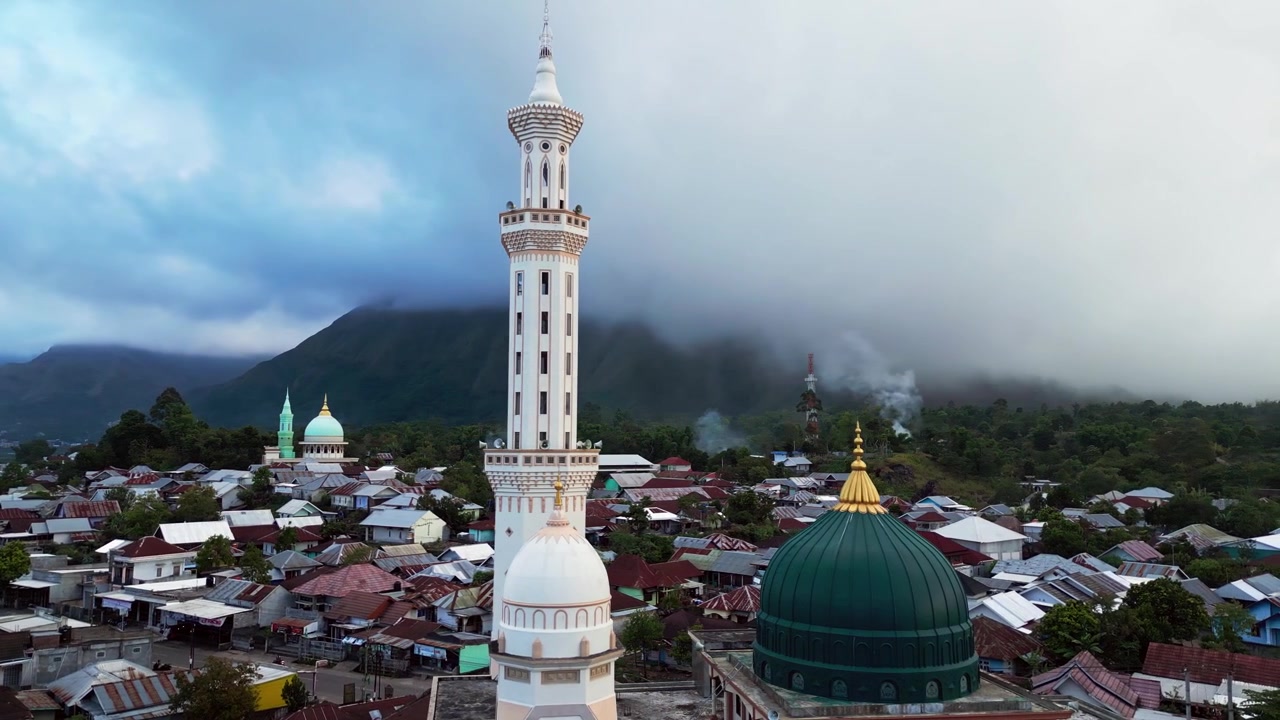 Masjid Islam dan menara tinggi menghadap desa pegunungan pedesaan di bawah latar belakang pegunungan yang dramatis, rekaman drone udara.