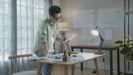 vista lateral del diseñador asiático con la tela pensando mientras mira el enlace de diseño en la oficina