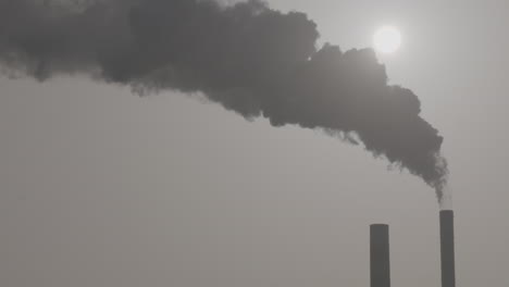 disparo de cámara lenta de humo industrial de una chimenea subiendo en el aire con el sol brillando a través del registro de fondo