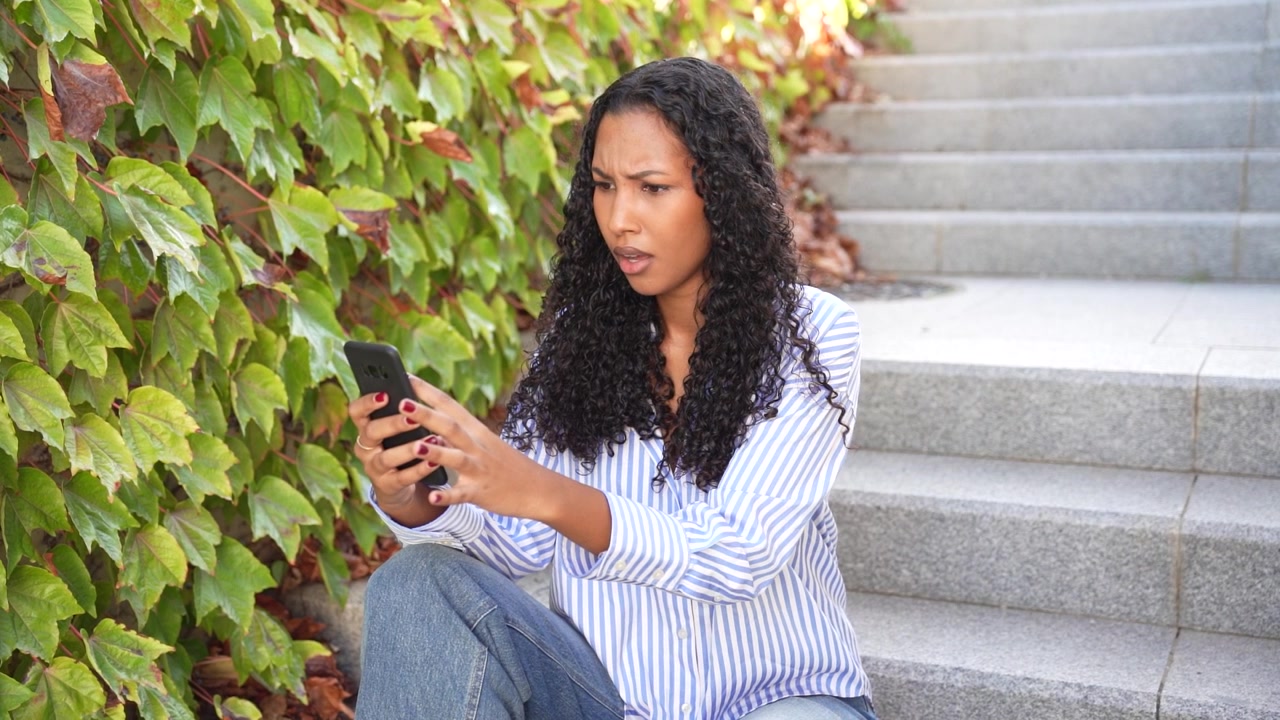A focused young woman is using her smartphone outdoors surrounded by lush green ivy
