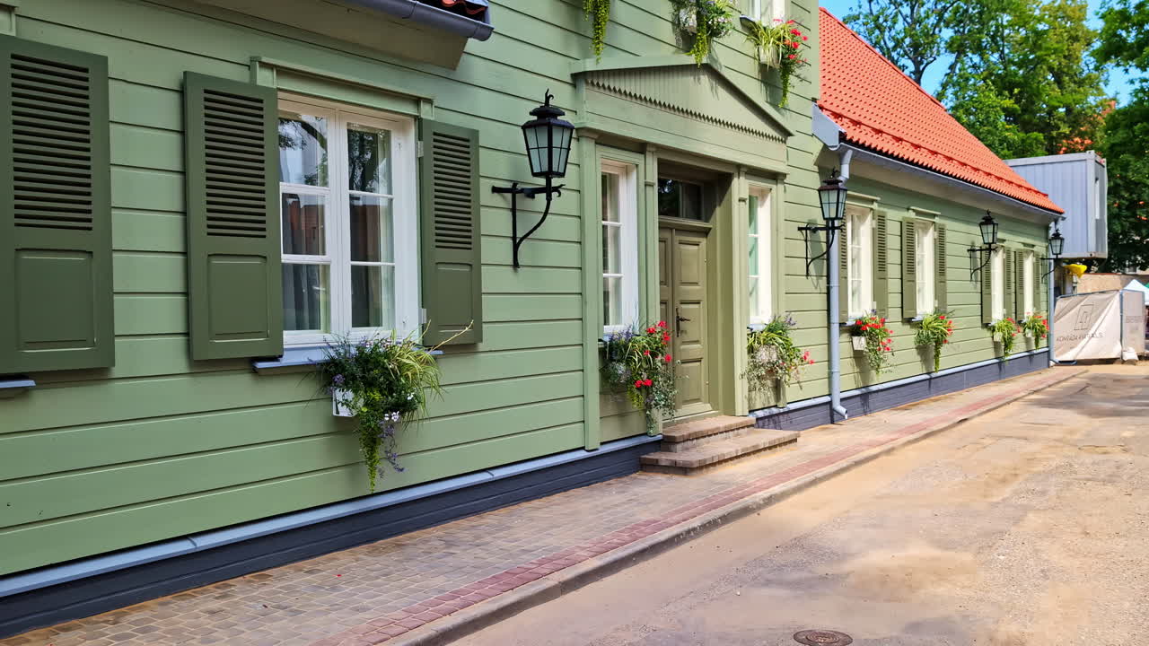 Classic green wooden villa with white windows, flower boxes and traditional shutters glows under summer sun in peaceful Jūrmala street