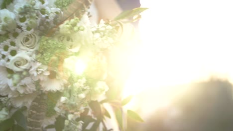 Bride-holding-a-wedding-bouquet-during-sunset,-beautiful-flare