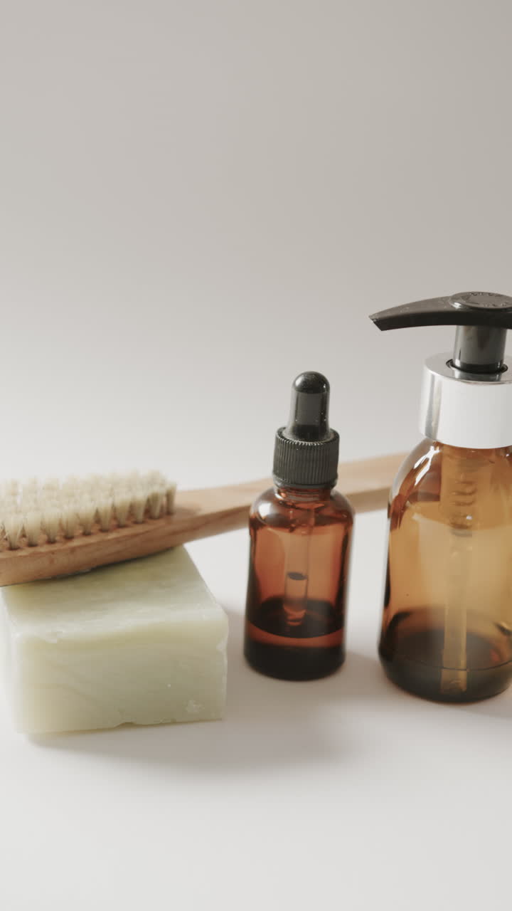Vertical video of close up of glass bottles, soap and brush and copy space on beige background